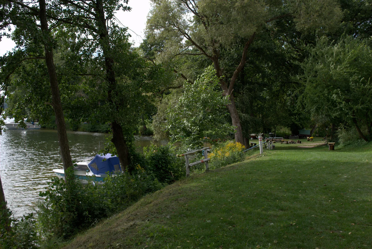 Ein am Ufer vertäutes Motorboot und ein gemähter Rasen mit Picknickplatz am Ukiel-See.
