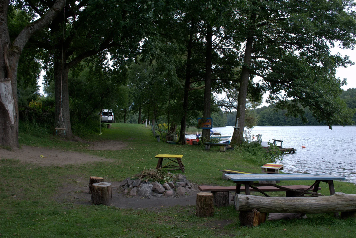 Eine Feuerstelle mit Baumstumpfsitzen, Picknicktische und eine Seilschaukel auf der Wiese am Ufer des Ukiel-Sees.